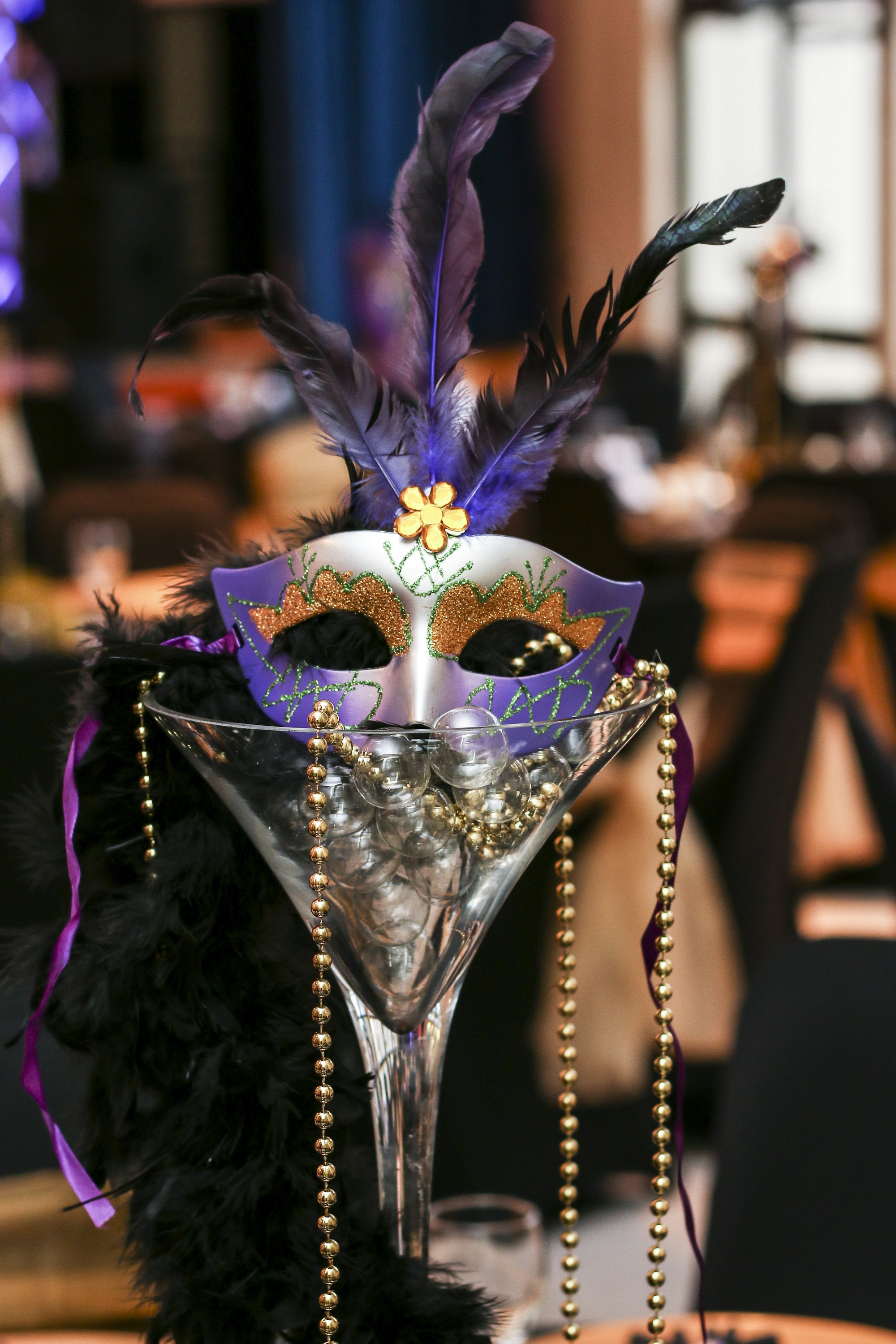 A purple, gold, and green feathered Mardi Gras mask draped with beads
