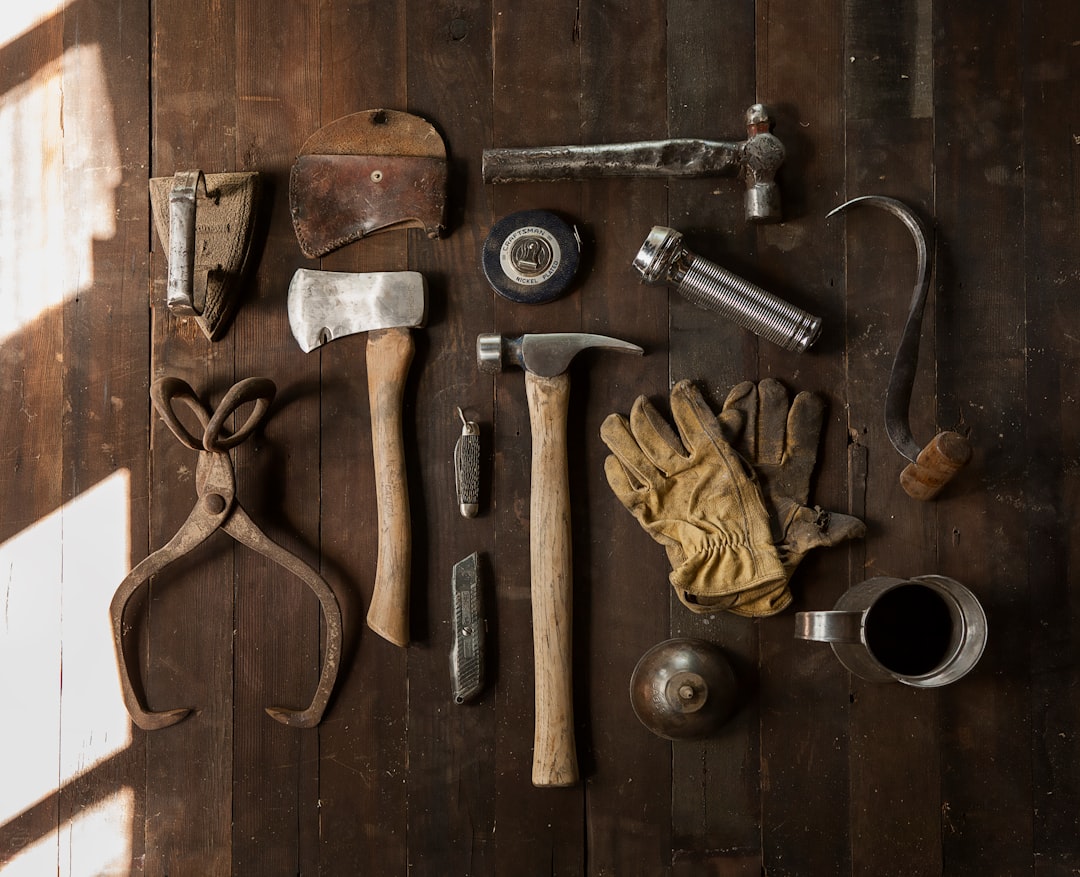 Vintage tools including an axe, hammer, gloves, and metal implements on dark wooden planks