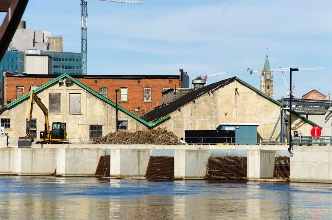 Urban riverfront with historic buildings, construction equipment, and city skyline.