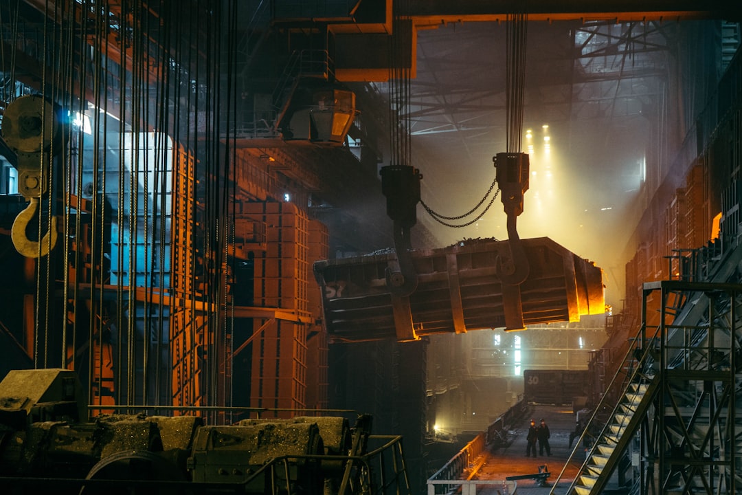 A heavy industrial crane lifting a glowing molten metal ladle in a steel mill