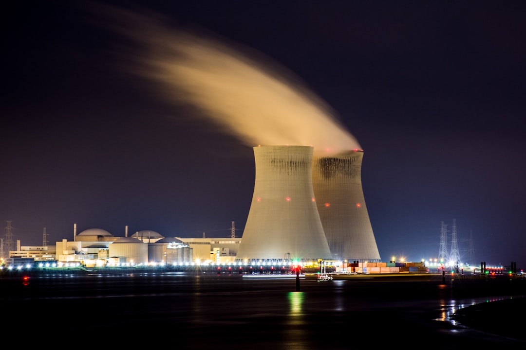 Two nuclear cooling towers emitting steam at night beside a dark river