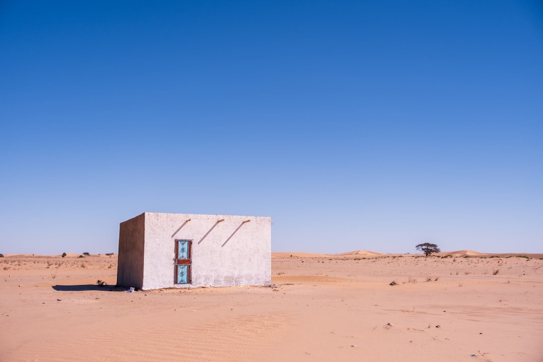 Lone building in sandy desert under clear blue sky.